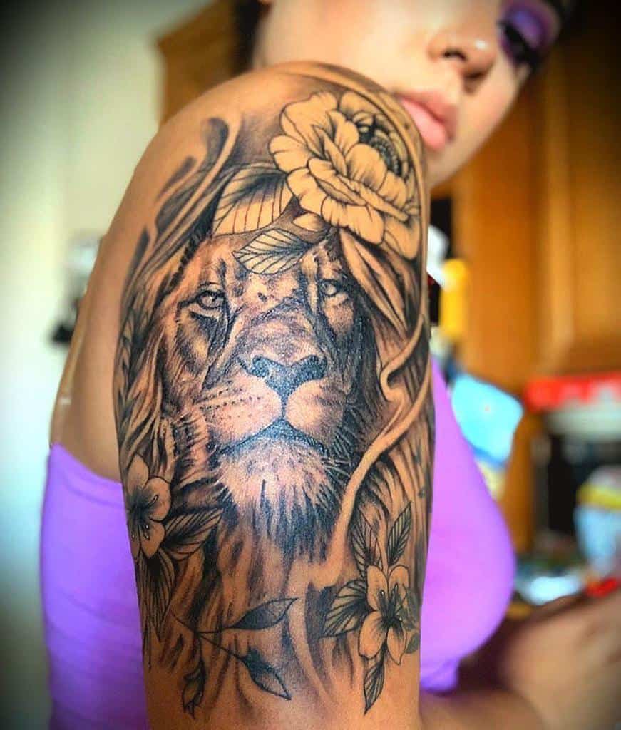Upper arm tattoo of a lion surrounded by roses and leaves
