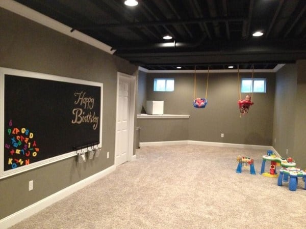 Basement playroom with dark exposed ceiling, chalkboard, and recessed spotlights.