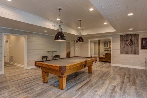 Spacious basement with pool table, wood panel walls, and large industrial-style pendant lights.
