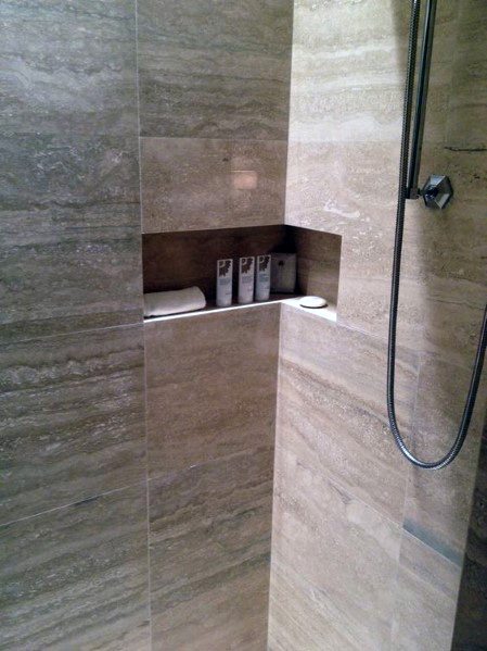 Corner shower with beige marble tiles, recessed shelf for bath products, and a sleek chrome showerhead