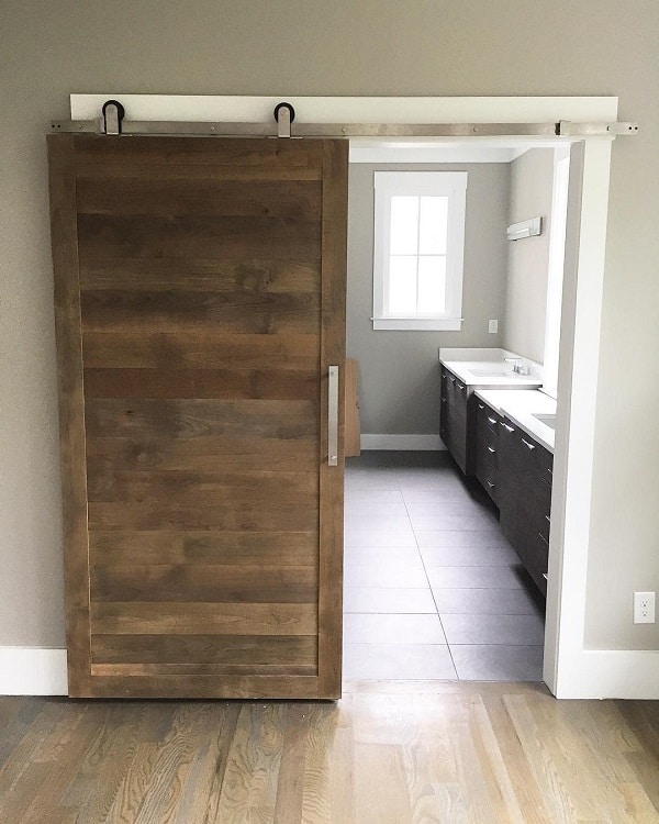 Reclaimed wood sliding barn door leading to a modern bathroom with dark cabinetry and light countertops.