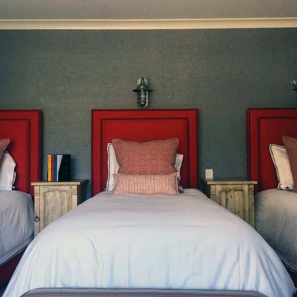 Three beds with striking red headboards, beige pillows, wooden bedside tables, and a lamp on the wall above