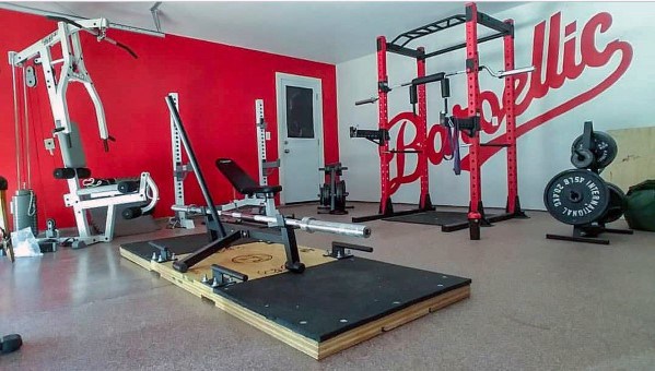 Garage gym with red and white decor, weightlifting platform, and squat rack station.