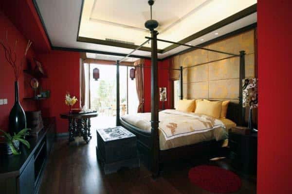 Luxurious bedroom with a four-poster bed, elegant decor, and natural light from large windows on red walls