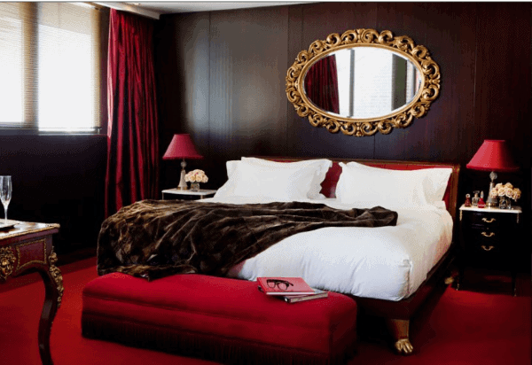 Luxurious bedroom with red decor, an ornate mirror, and elegant furnishings featuring a plush bed and side tables