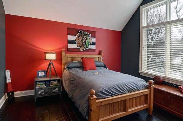 Bedroom with red and gray walls, wooden bed, and sports-themed painting above the red-accented headboard