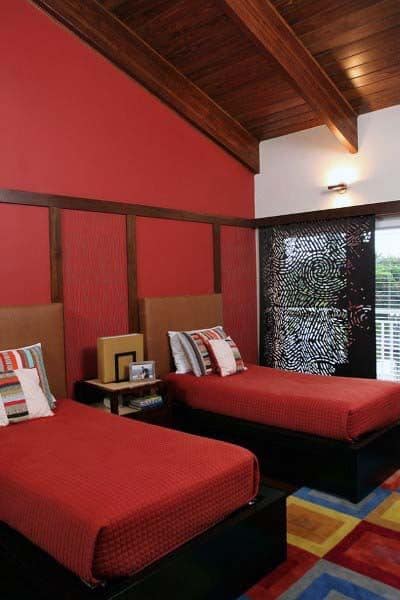 Twin beds with red bedding in a room showcasing a wooden ceiling and an artistic partition wall