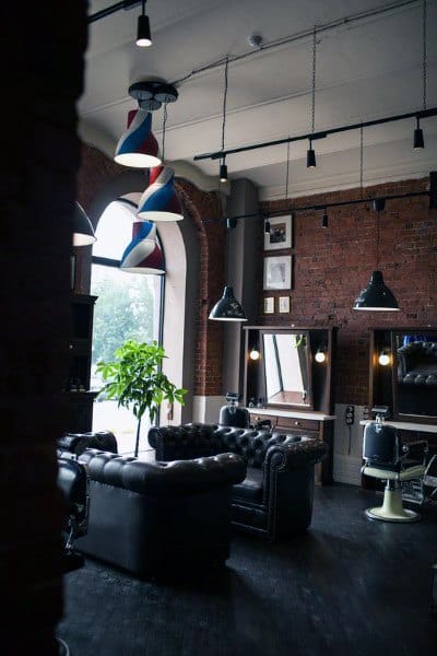 Industrial barbershop with red brick walls, leather sofa, and arched windows.