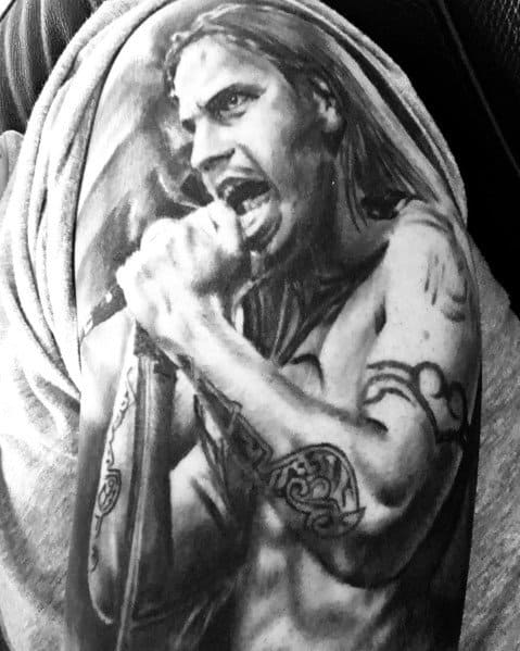 Realistic black and grey upper arm tattoo of a long-haired singer gripping a microphone, capturing an intense live performance energy.