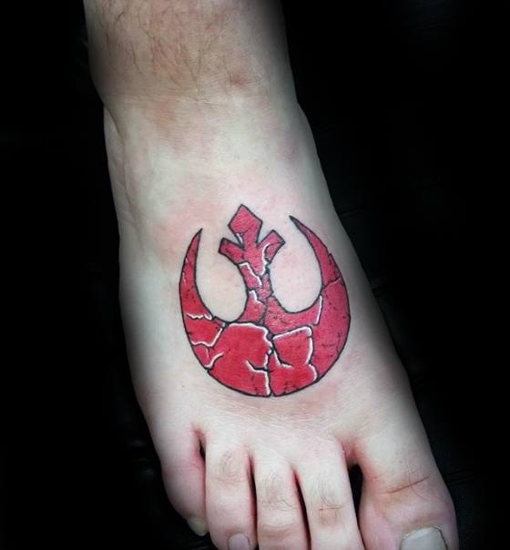 Cracked red Rebel Alliance tattoo on the top of the foot, with a textured stone-like appearance.
