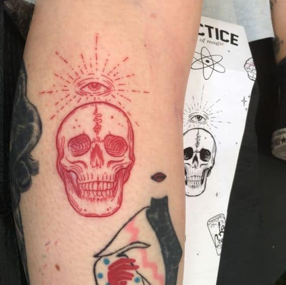 Tattoo of a red skull with a third eye radiating light, inked in fine lines on the forearm.