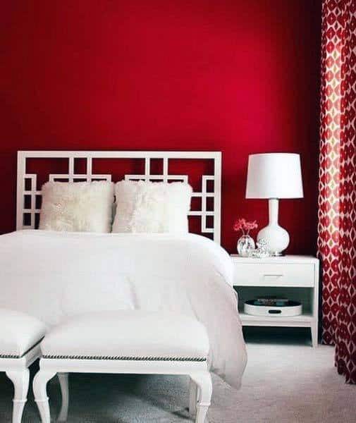 Bedroom with bold red walls, white bed, nightstand, and red patterned curtains for a stylish red-accented decor