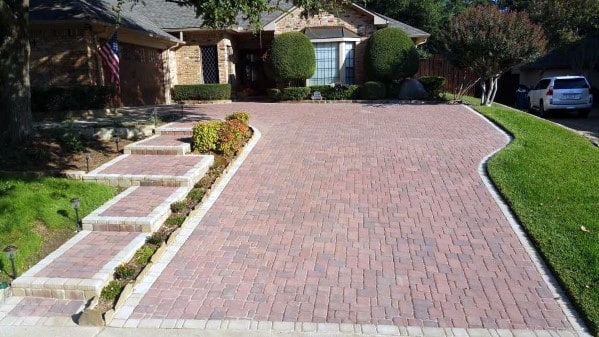 Red paver driveway with light brick edging and matching steps leading to a brick house.