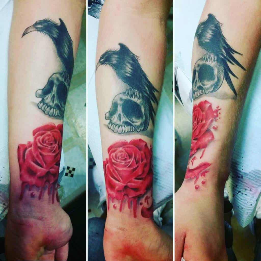 Forearm tattoo featuring a black raven perched on a skull with a vivid red rose dripping like blood, creating a dark and dramatic design.