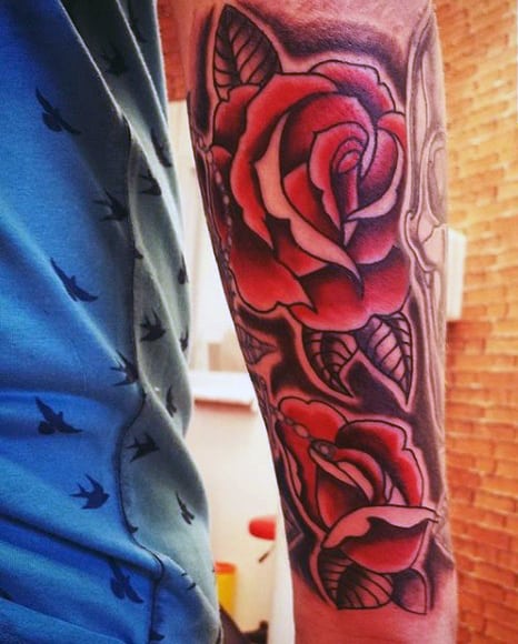 Close-up of an arm tattoo featuring vibrant red roses and leaves
