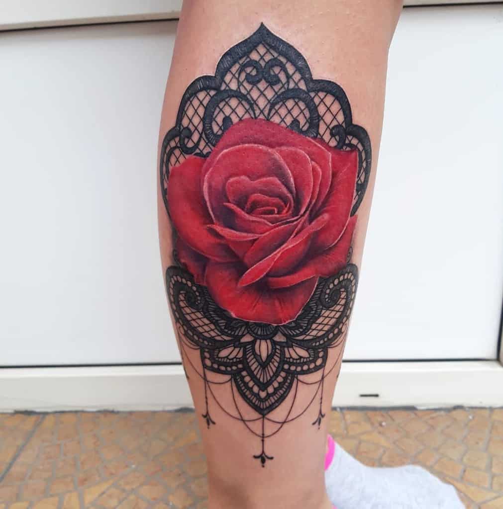 Leg tattoo featuring a bold red rose with intricate black lace patterns, ornamental filigree, and delicate beaded chain details.