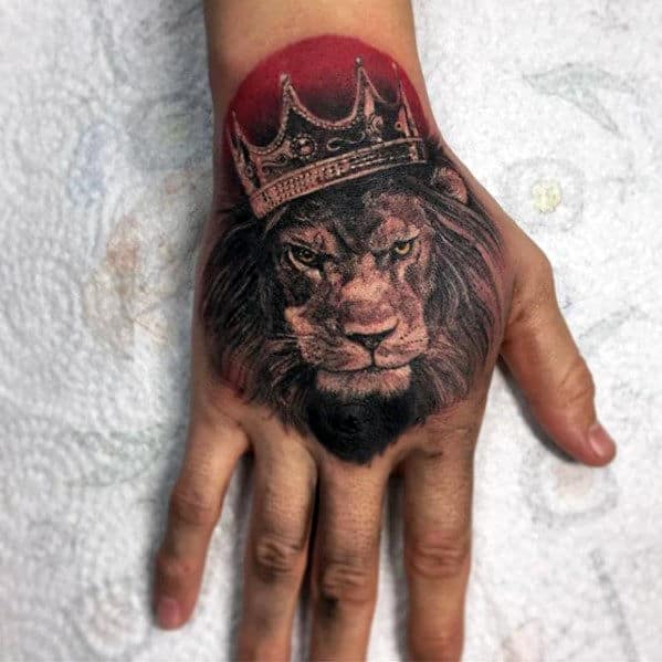 A hand with a detailed tattoo of a lion wearing a crown on the back of it