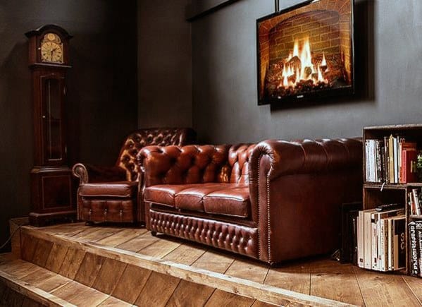 Red tufted leather sofa and armchair on a wooden platform with a fireplace and grandfather clock.