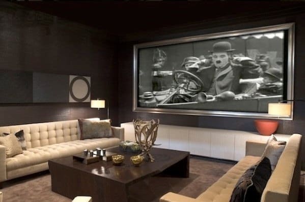 A luxurious home theater with a large screen showing a black-and-white film, featuring two beige couches and decor