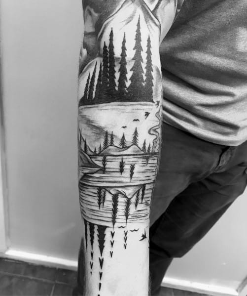 Tattoo of a mountain landscape with trees reflected in a lake, featuring fine lines and symmetry for a peaceful and nature-inspired design.