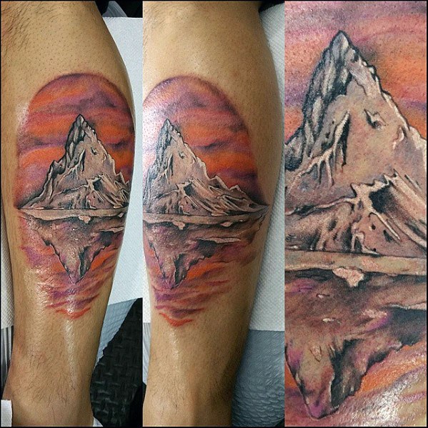 Tattoo of a towering mountain reflecting in a lake, set against a vibrant sunset sky, creating a bold and scenic nature-inspired design.