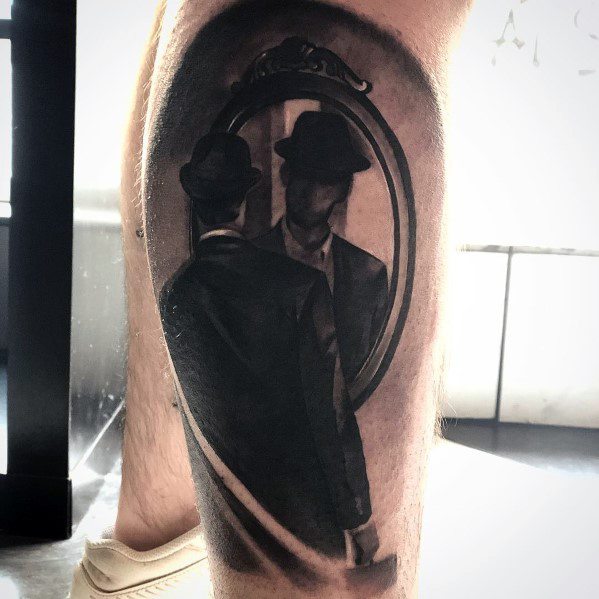Tattoo of a man in a suit looking into a mirror, with his reflection mysteriously facing away, creating a surreal and thought-provoking design.