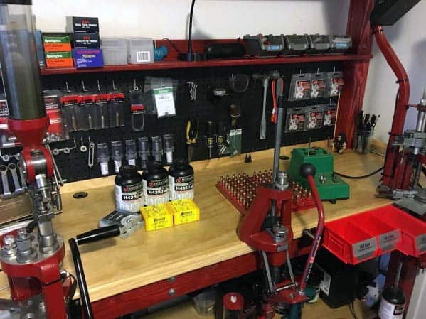 Reloading bench with red presses, organized pegboard tools, reloading supplies, and a clean wooden work surface