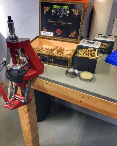 Simple reloading bench with a red press, brass casings organized in boxes, and tools neatly arranged for precision work