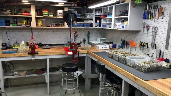 Spacious reloading bench setup with red presses, organized tools on pegboards, and labeled bins for brass and components