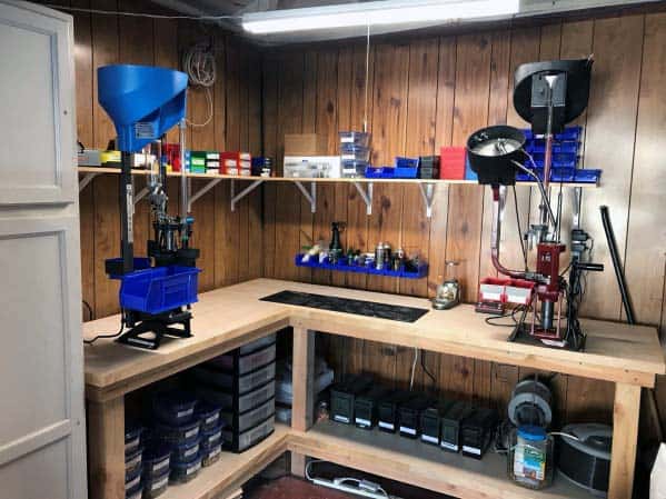 Corner reloading bench with mounted blue and red presses, organized storage bins, and wooden shelves for tools and supplies