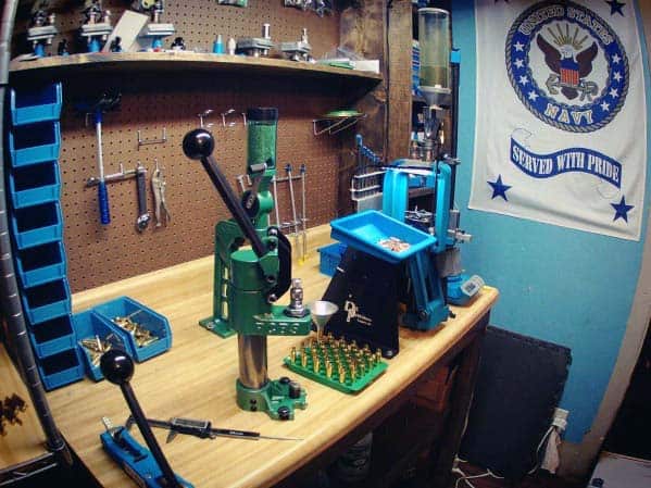 Efficient reloading bench with mounted green and blue presses, organized tools on pegboard, and a U.S. Navy-themed backdrop