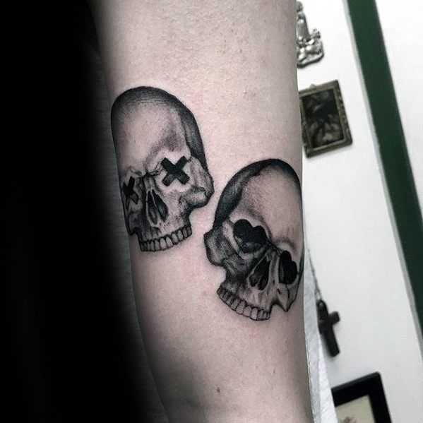 Tattoo of two shaded skulls—one with X eyes and the other with heart eyes—blending dark art with punk-inspired Green Day symbolism.