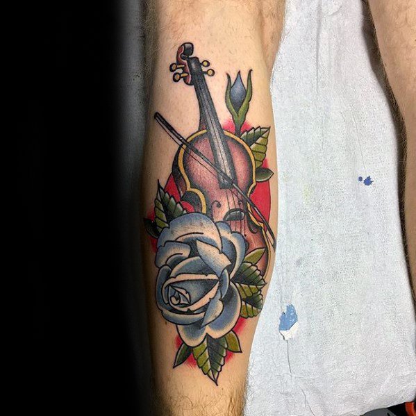 Traditional-style tattoo of a violin with a white rose and green leaves, framed by a bold red background and clean black outlines on the forearm.
