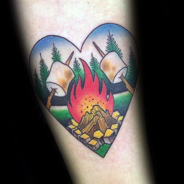 Heart-shaped campfire tattoo with glowing flames, toasted marshmallows on sticks, pine trees, and a clear blue sky in a colorful design.