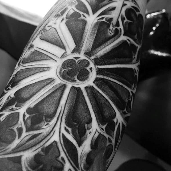 Close-up tattoo of a gothic rose window with bold black shading and crisp white highlights, creating a dramatic stained glass effect.