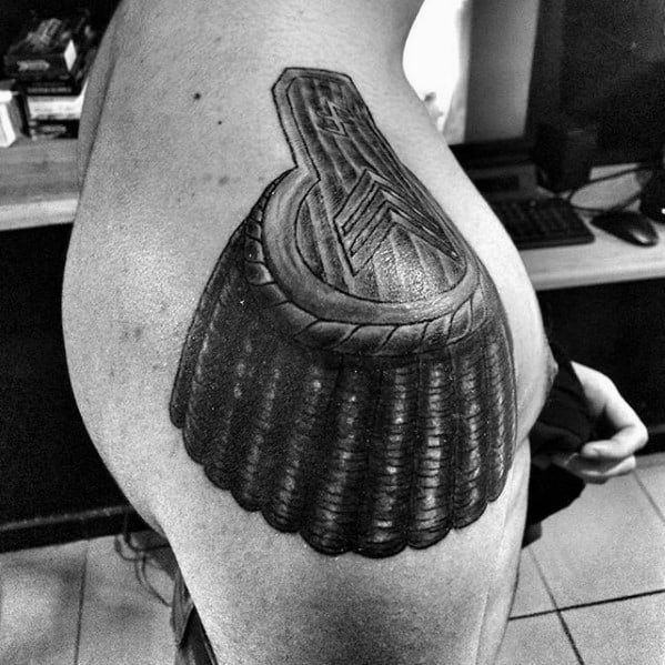 Bold epaulette tattoo with deep shading, thick rope border, and layered plate-like tassels covering the upper arm.