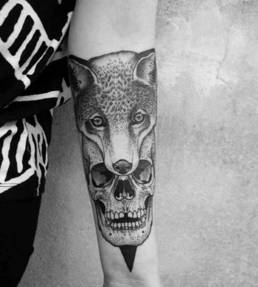Detailed black and grey forearm tattoo of a fox face seamlessly merging into a human skull, symbolizing duality and mystery.