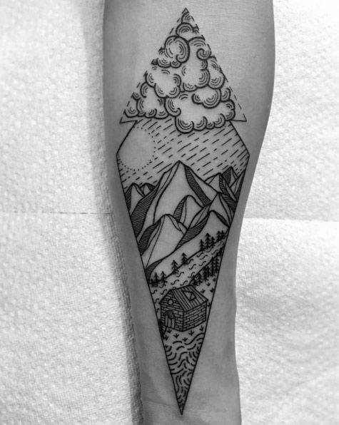 Detailed forearm tattoo in a tall diamond shape featuring clouds, mountains, a forest trail, and a cabin by a river.