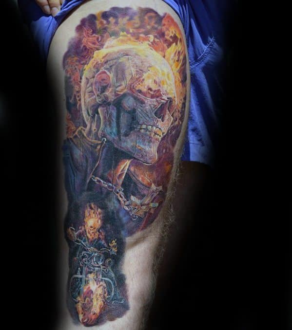 Large Ghost Rider thigh tattoo featuring a realistic flaming skull, fiery chain, and full-body rider on a burning motorcycle in dramatic tones.