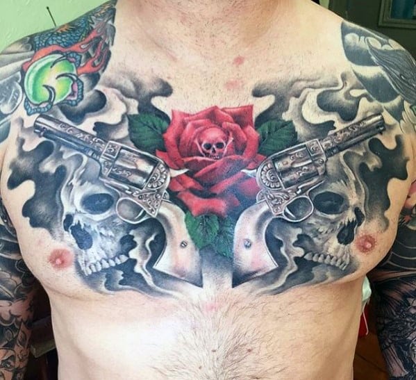 Chest tattoo with two detailed revolvers, skulls, and a central red rose with a tiny skull inside, surrounded by black smoke-like shading.