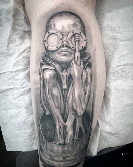 HR Giger-inspired tattoo of a surreal humanoid figure with large goggles, elongated limbs, and biomechanical tubing in a fetal-like pose.