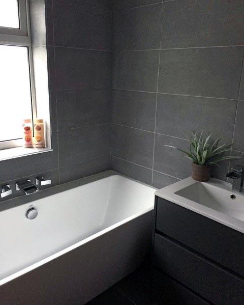 A gray bathroom featuring subway tiles, a sleek glass shower divider, and a compact tub for a clean and modern look.