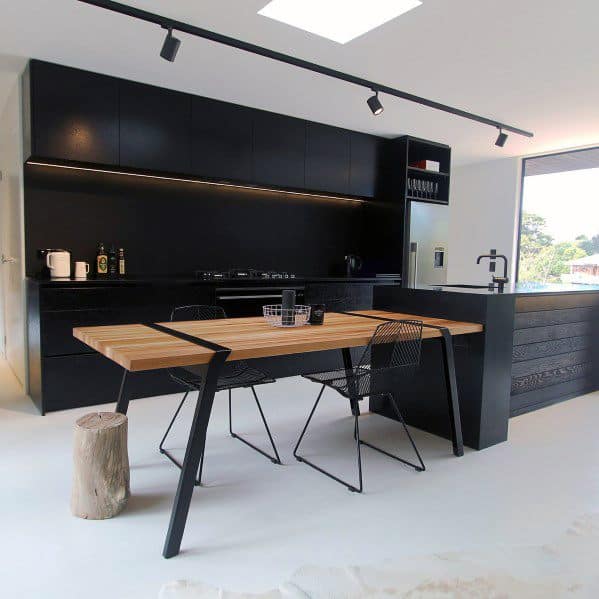 Minimalist black kitchen with wooden dining table, track lighting, and open layout design.