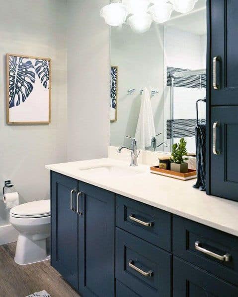 Bathroom with navy blue vanity, white countertop, large mirror, and framed leaf artwork.