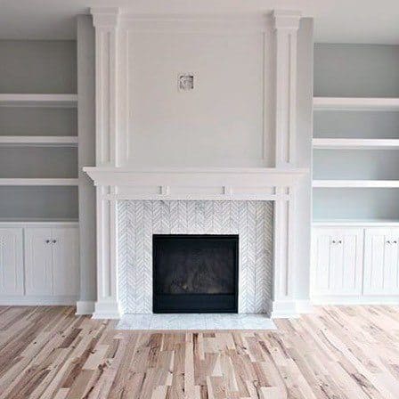 Minimalist built-in bookcases flanking a white fireplace with herringbone tile detail, creating a bright and clean focal point in the room