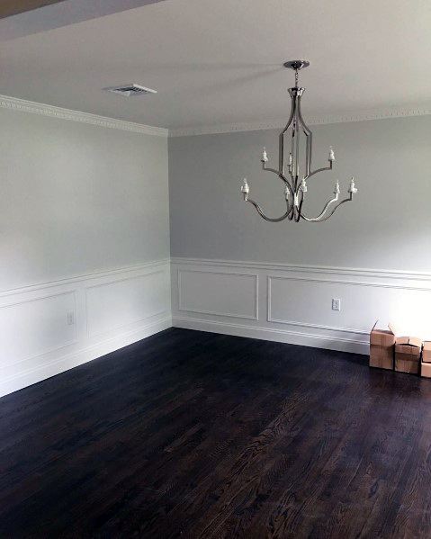Empty room with dark wooden floor, white walls featuring a chair rail, a silver chandelier, and cardboard boxes in the corner
