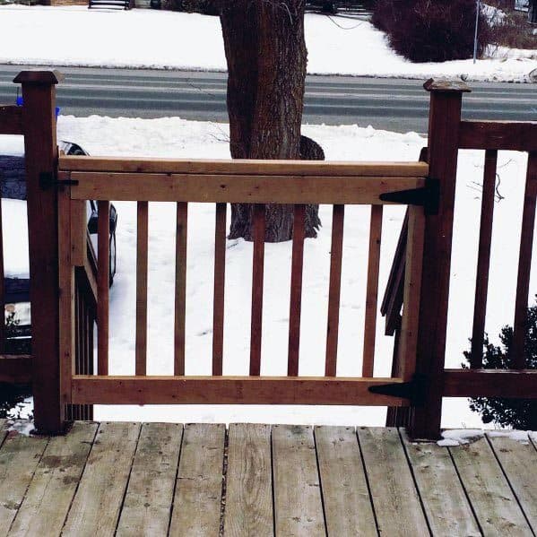 A wooden gate on a snowy deck overlooks a road and bare tree