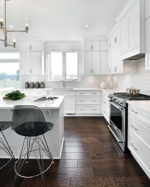 White kitchen with dark wood flooring, modern island, and transparent bar stools.