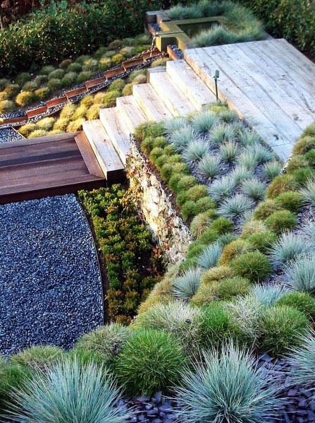 Modern sloped landscaping with tiered stone steps, ornamental grasses, gravel pathways, and clean geometric lines for a contemporary look