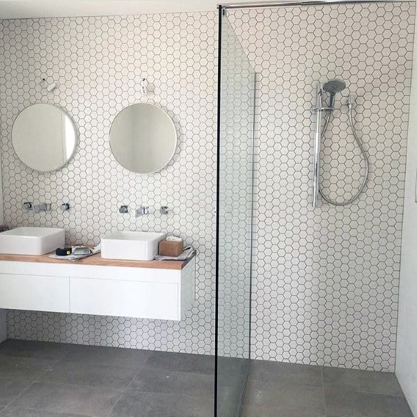 Minimalist white bathroom with double sinks, round mirrors, and a glass shower enclosure